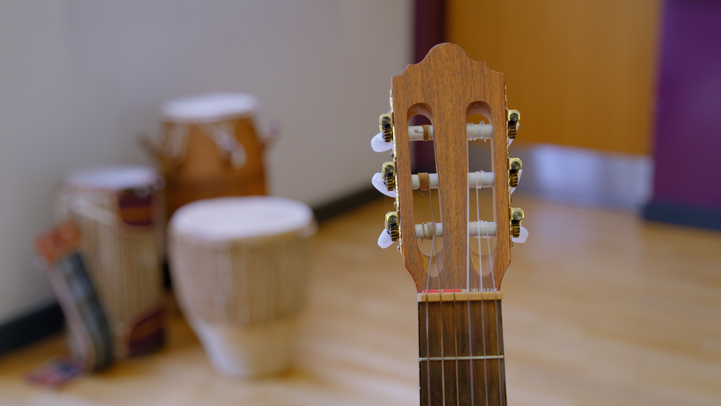 Classical guitar headstock in the foreground with drums softly blurred behind