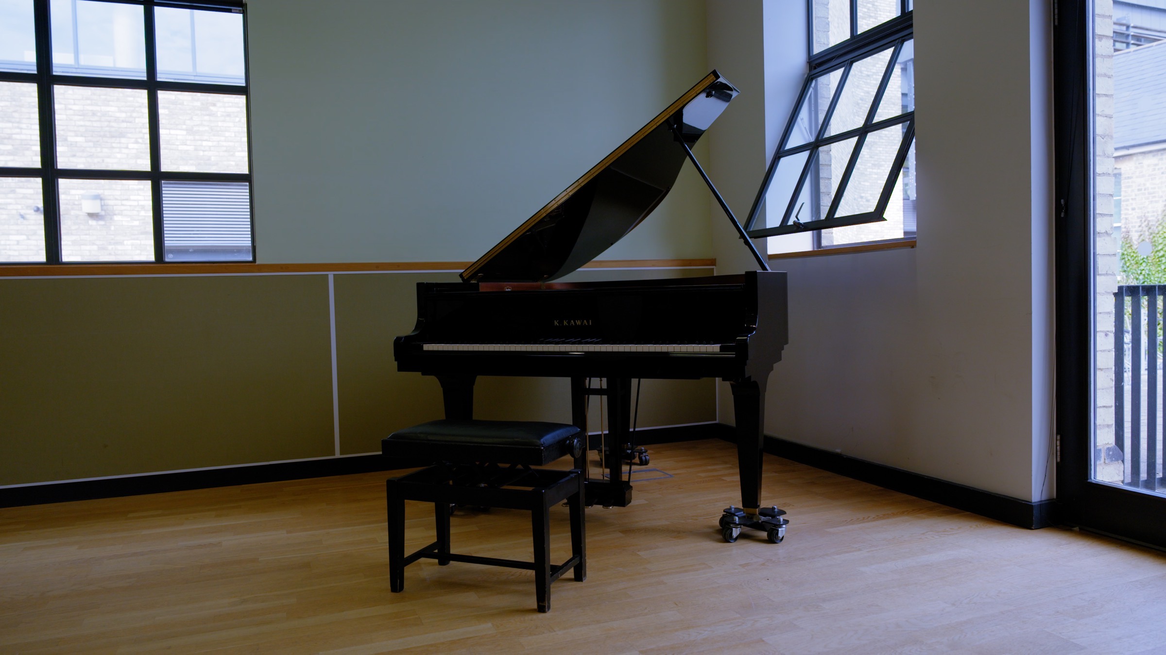 A black grand piano in a bright therapy room with green walls and natural light in Walthamstow, London